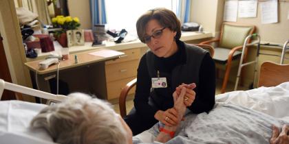 Rabbi Sara Paasche-Orlow sits in a chair and holds a patients hand while talking to her