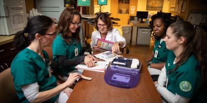 A group of nursing students sit around a table to learn from a Hebrew SeniorLife employee