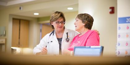 A Hebrew SeniorLife doctor puts her arm around a woman as she stands and talks with her