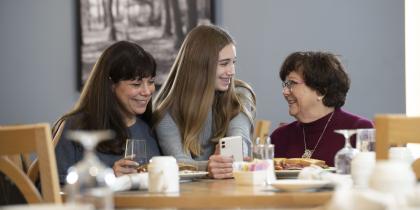Grandmother, mother, and daughter sitting at a dinner table and looking at the daughter's cell phone.