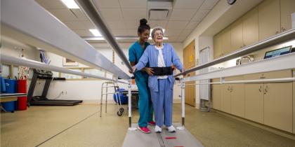 young nurse guiding an elderly patient to walk with guiderail assistance during physical rehabilitation