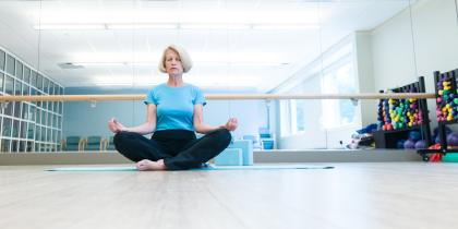 Woman in aqua blue shirt sitting cross-legged, in a meditative pose with the back of her hands on her knees.