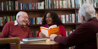Three seniors converse around a table in a library.