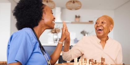A visiting nurse and an older adult woman share a high five.