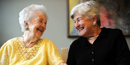 Two older women sitting together smiling.