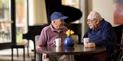 Two older men sitting together at a table in a lounge area.
