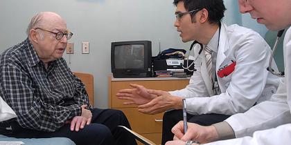 Older man sitting and talking with two doctors.