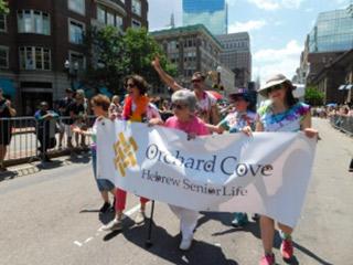 A group of HSL employees and residents walk in the Boston Pride Parade while holding an Orchard Cove banner.