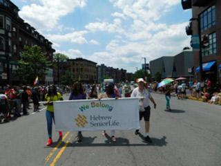 A group of HSL employees and residents walk in the Boston Pride Parade holding a sign that says "We Belong".
