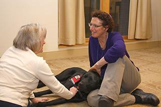 Rabbi Karen Landy and Tamari, her ministry service dog, sit on the floor with an elder woman