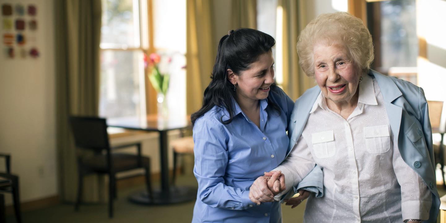 A resident of assisted living at NewBridge on the Charles receives help with the tasks of daily living in her apartment.