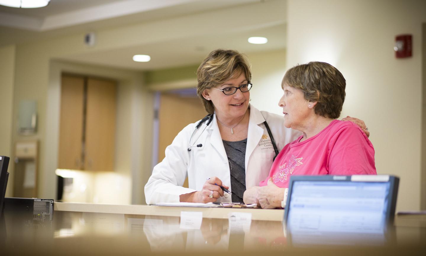 A female patient and female doctor stand talking in front of a counter at Hebrew Rehabilitation Center.