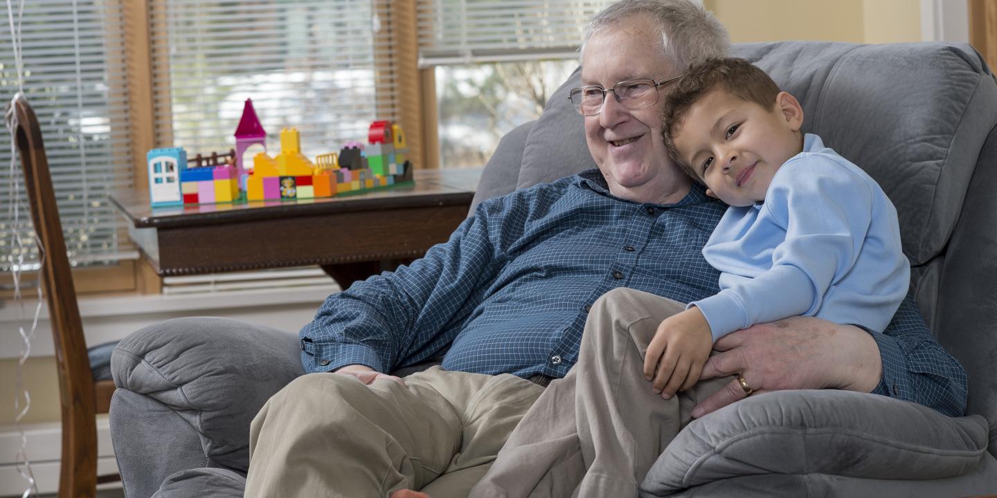 Smiling grandfather with grandson sitting on chair with toys on table in background