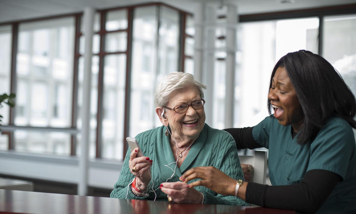 A patient at Hebrew Rehabilitation Center listens to therapeutic music with the help of a life enhancement team member.