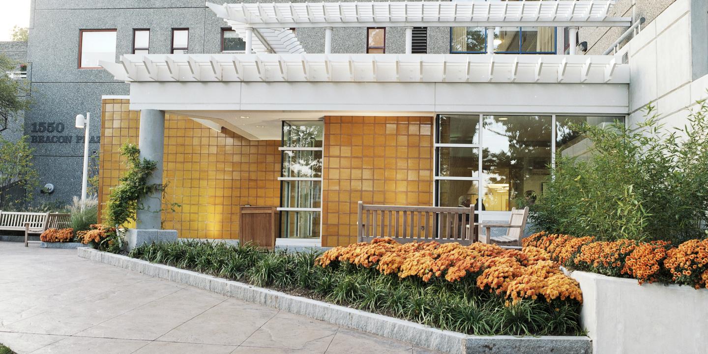 A path lined with orange flowers and green shrubs leads to the entrance of 1550 Beacon Street, part of Center Communities of Brookline.