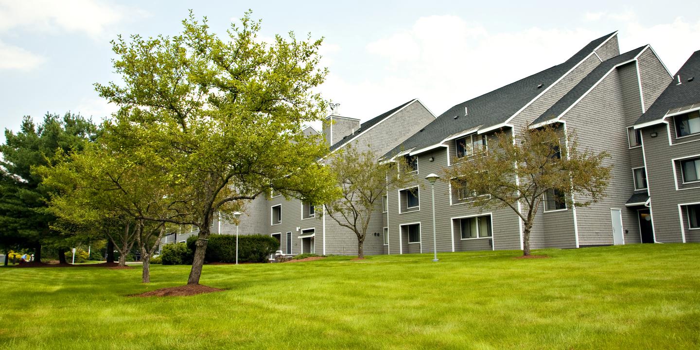 Exterior shot of three-story apartment complex surrounded by trees and grass.