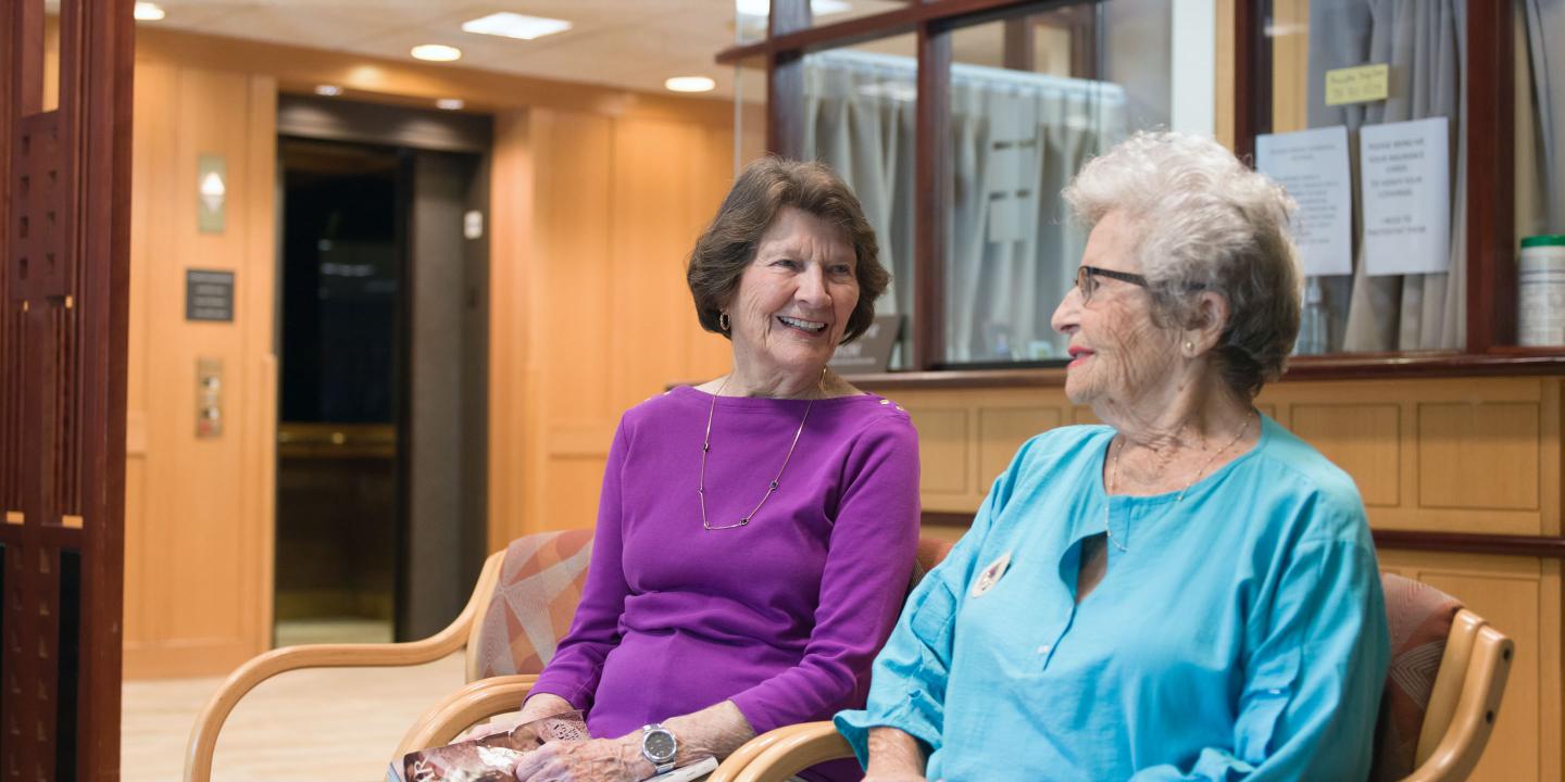 Two residents of Orchard Cove chat in the waiting area of the community’s Harvard Medical School-affiliated medical practice.