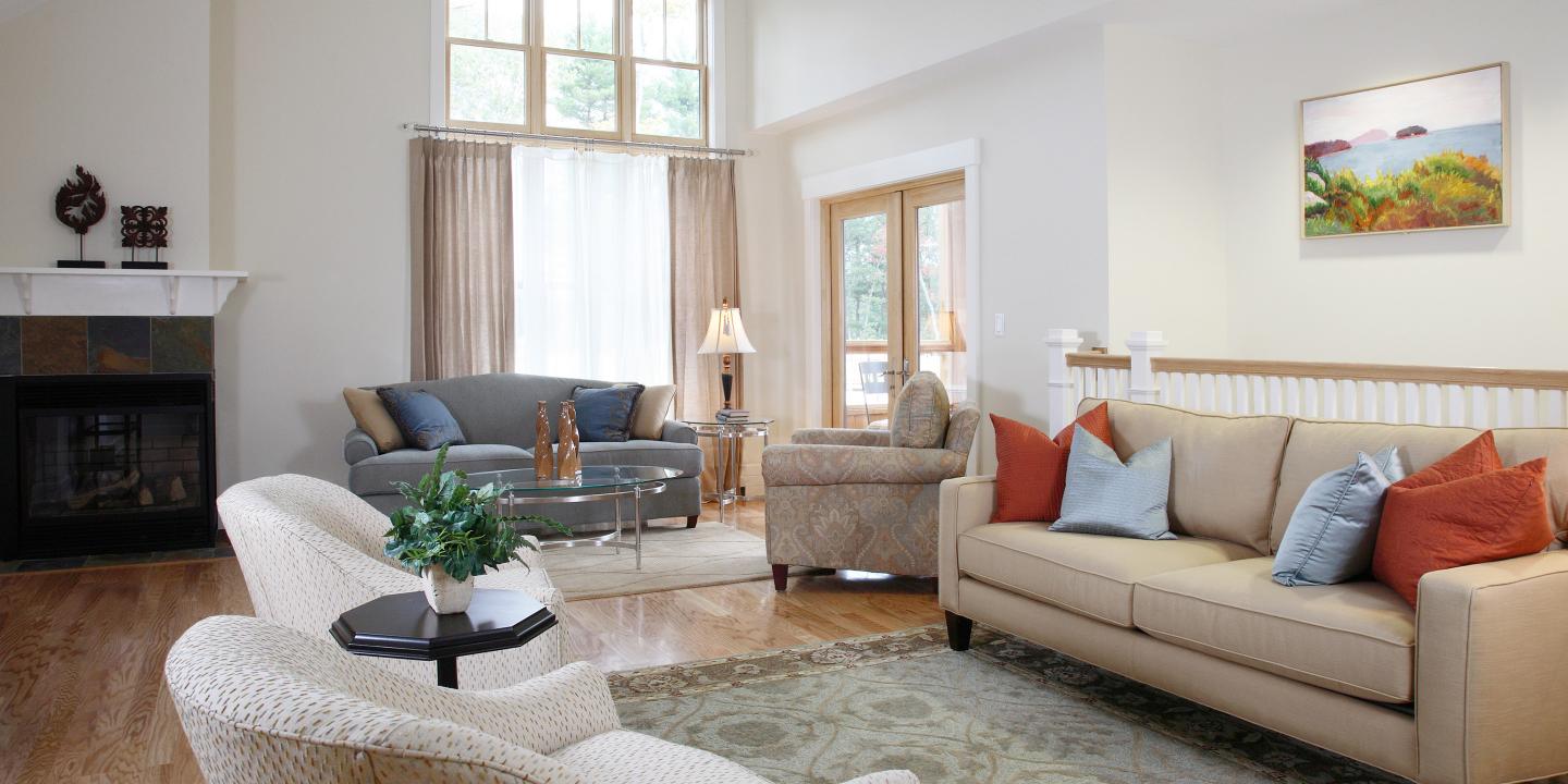 This spacious, sunny, and well-decorated living room with two seating areas is a typical independent living residence interior at NewBridge on the Charles.