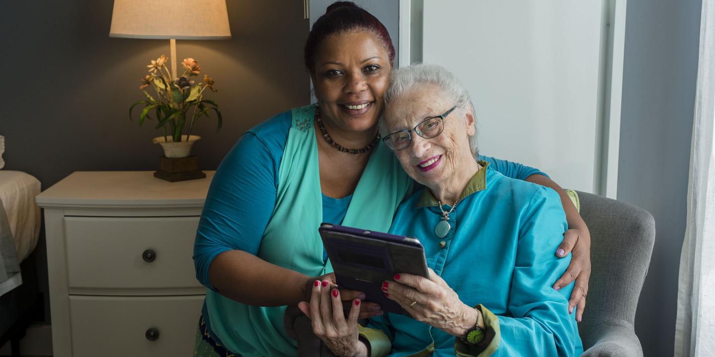 Smiling Hebrew SeniorLife staff with smiling older woman sharing photos