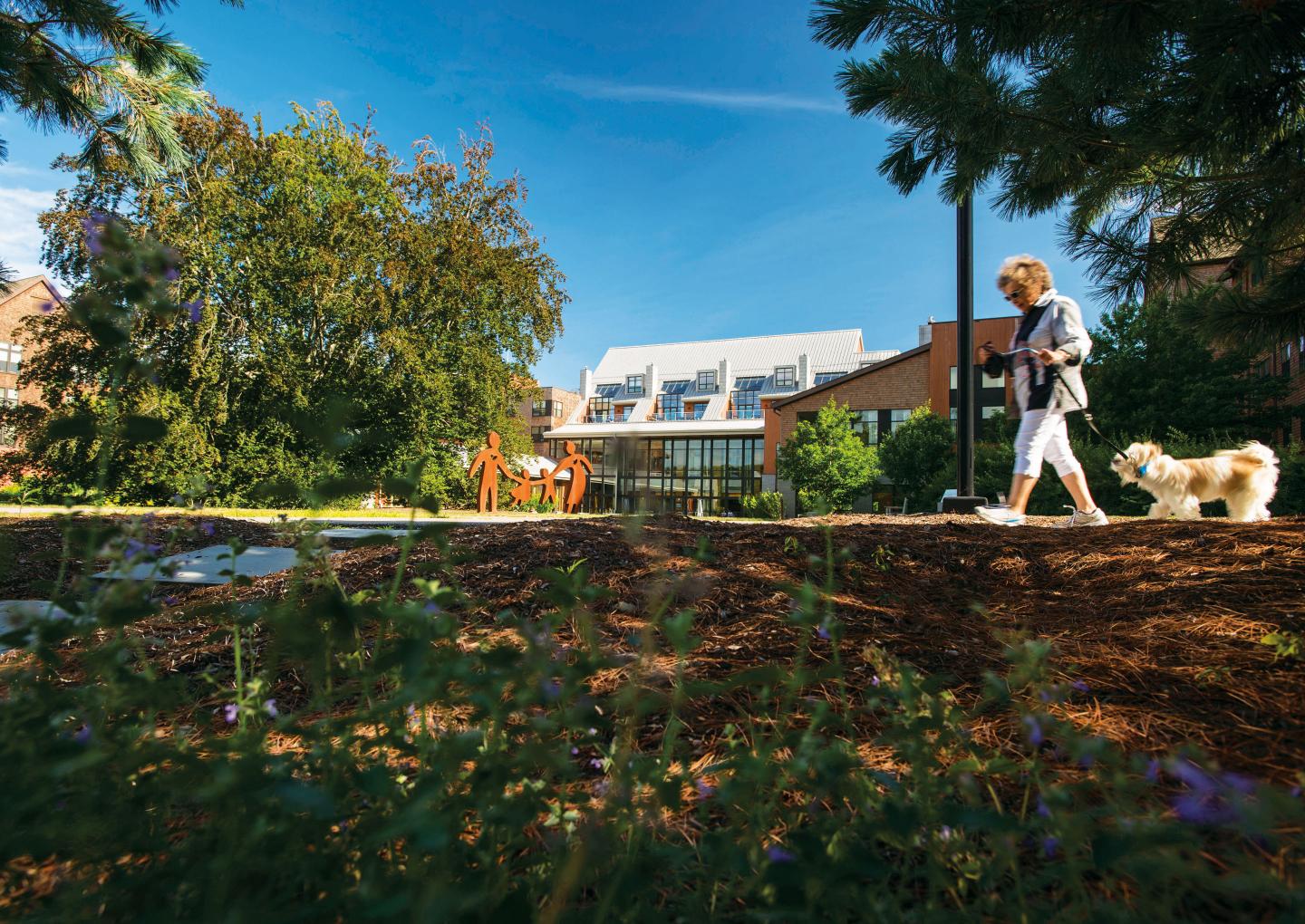 A NewBridge on the Charles resident walks her dog on a wooded trail that winds around the Shapiro Community Center.