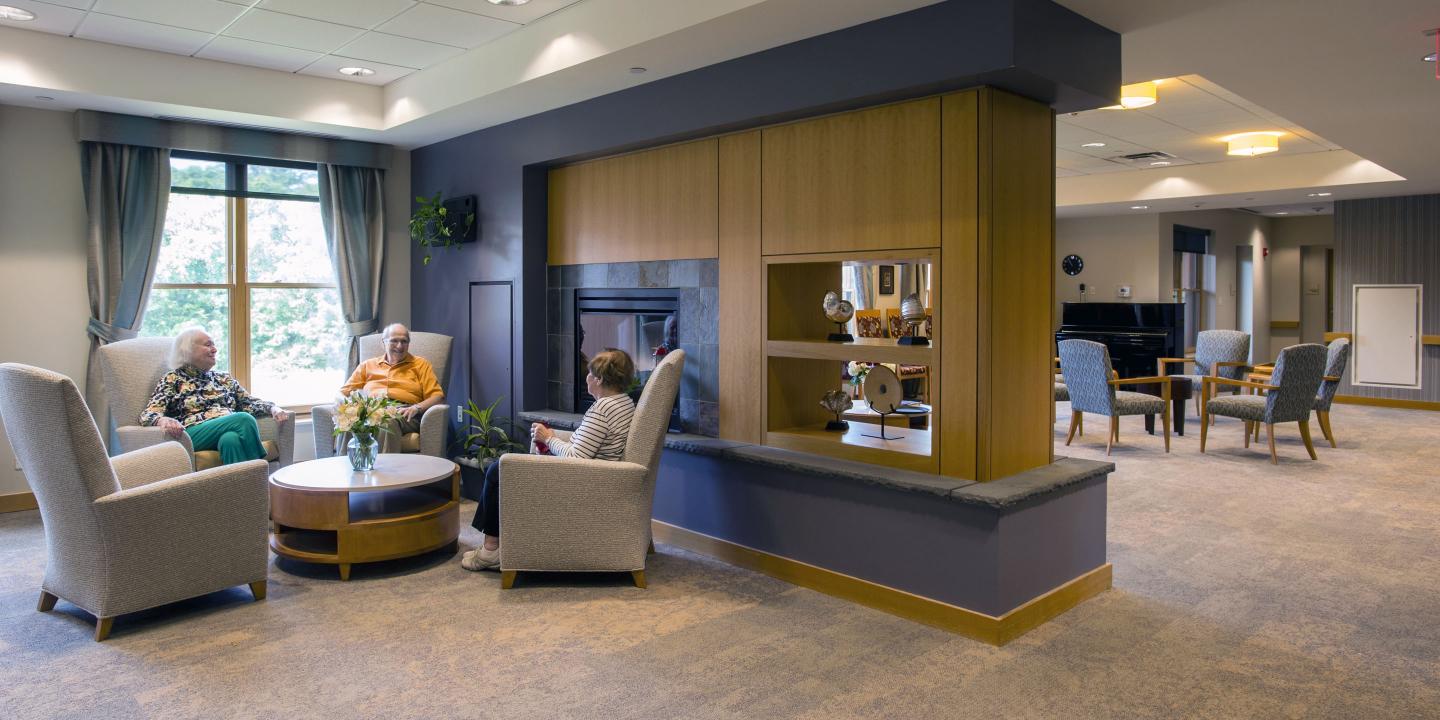 Three residents of Memory Care Assisted Living at NewBridge on the Charles enjoy a conversation in one of our spacious common areas, featuring contemporary décor and plenty of natural light.