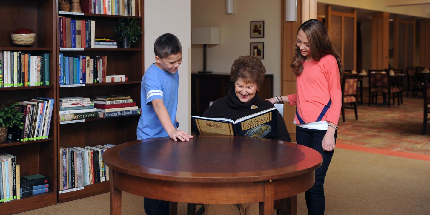 A resident reads together with students from the on-campus Rashi school in the NewBridge Assisted Living library
