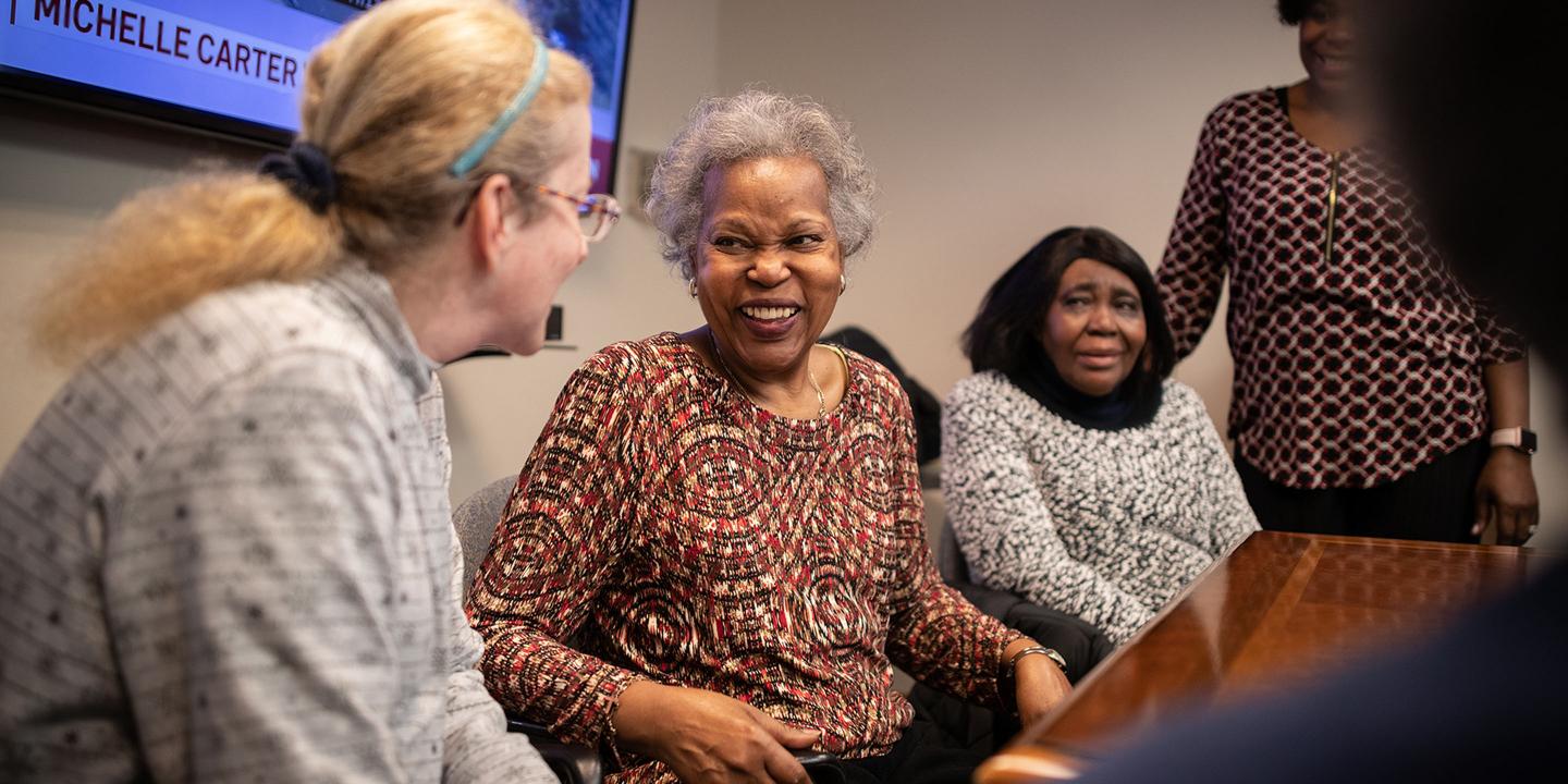 Three women sit chatting and laughing at Simon C. Fireman Community in Randolph, MA.