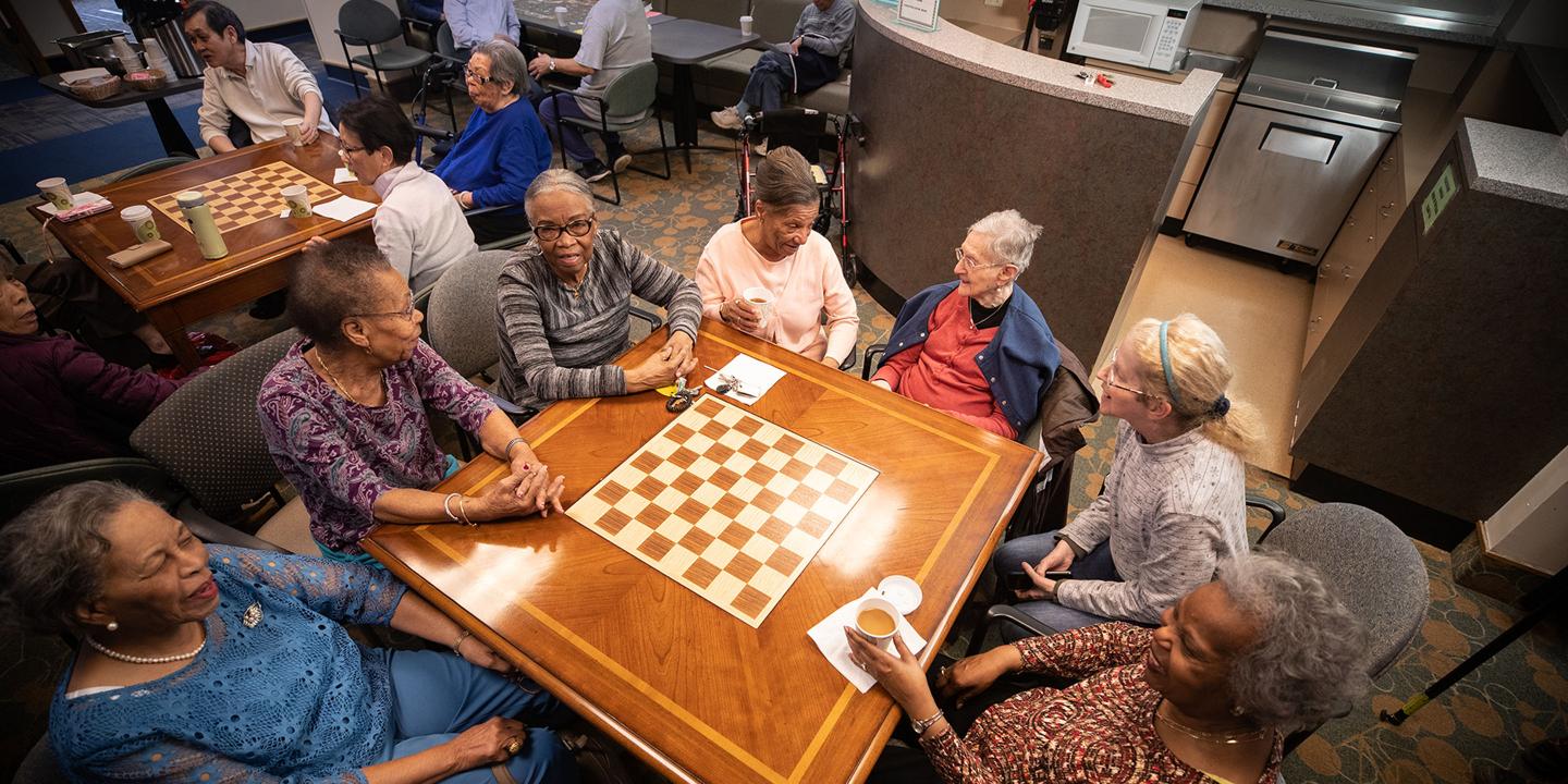 A diverse group of seniors sits at a table, laughing and chatting at Simon C. Fireman Community in Randolph, MA