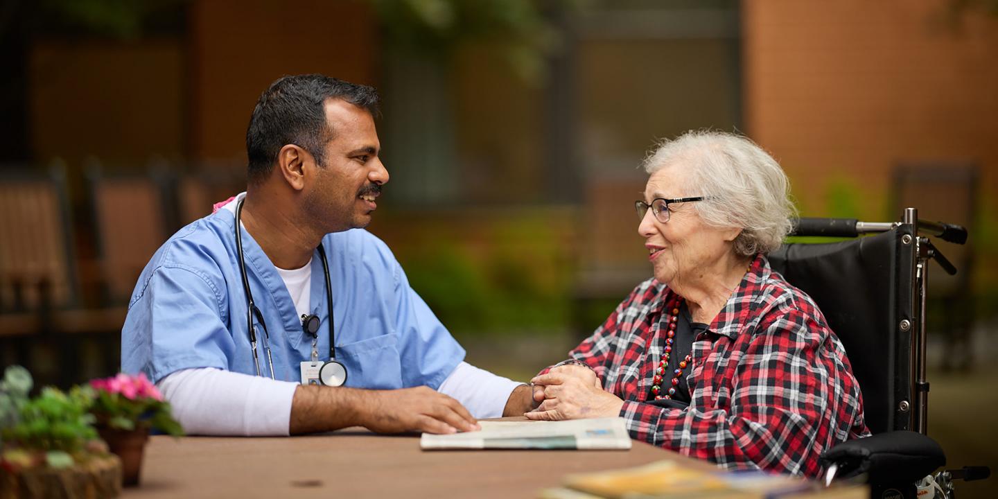 A male nurse and a female patient enjoying a conversation on an outside patio.