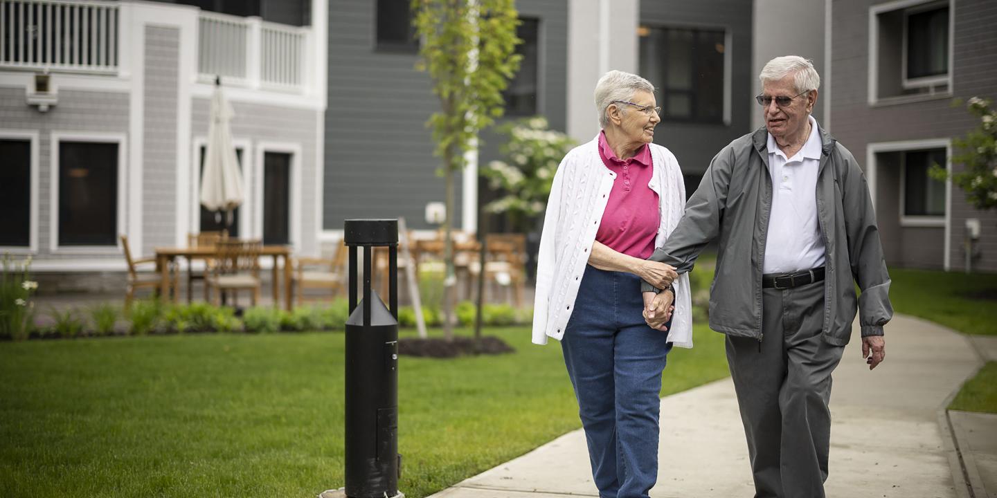An older couple walk hand-in-hand on walking path.