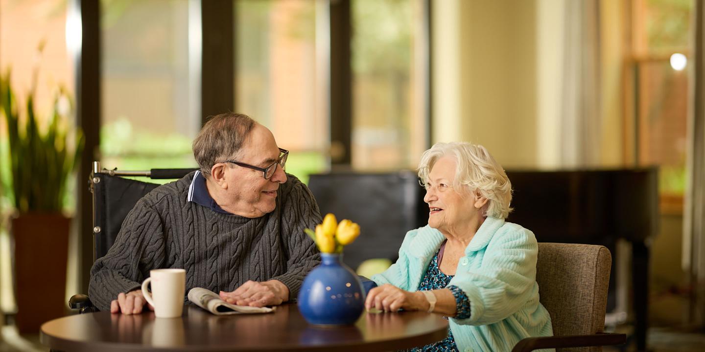 An older man and woman enjoy coffee and discussion at a table.