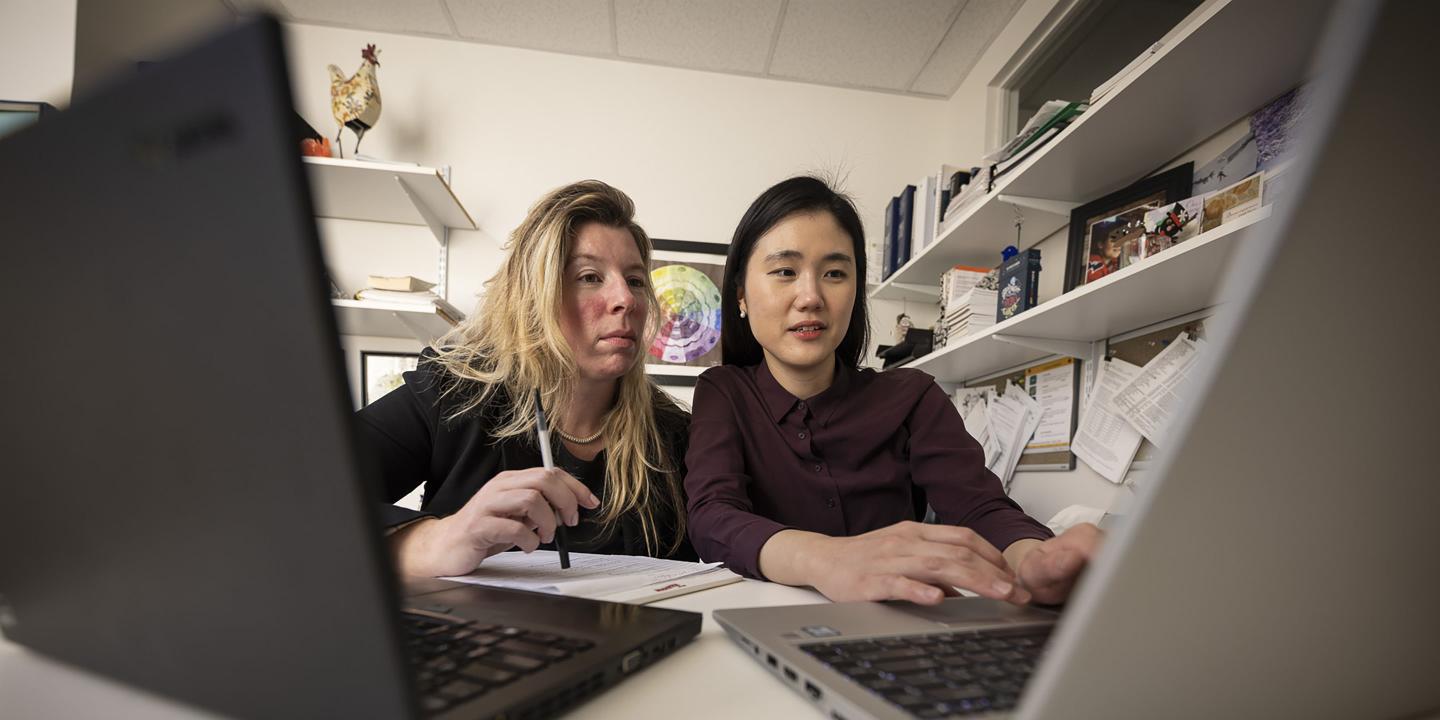 Two female researchers review data on computer screens.