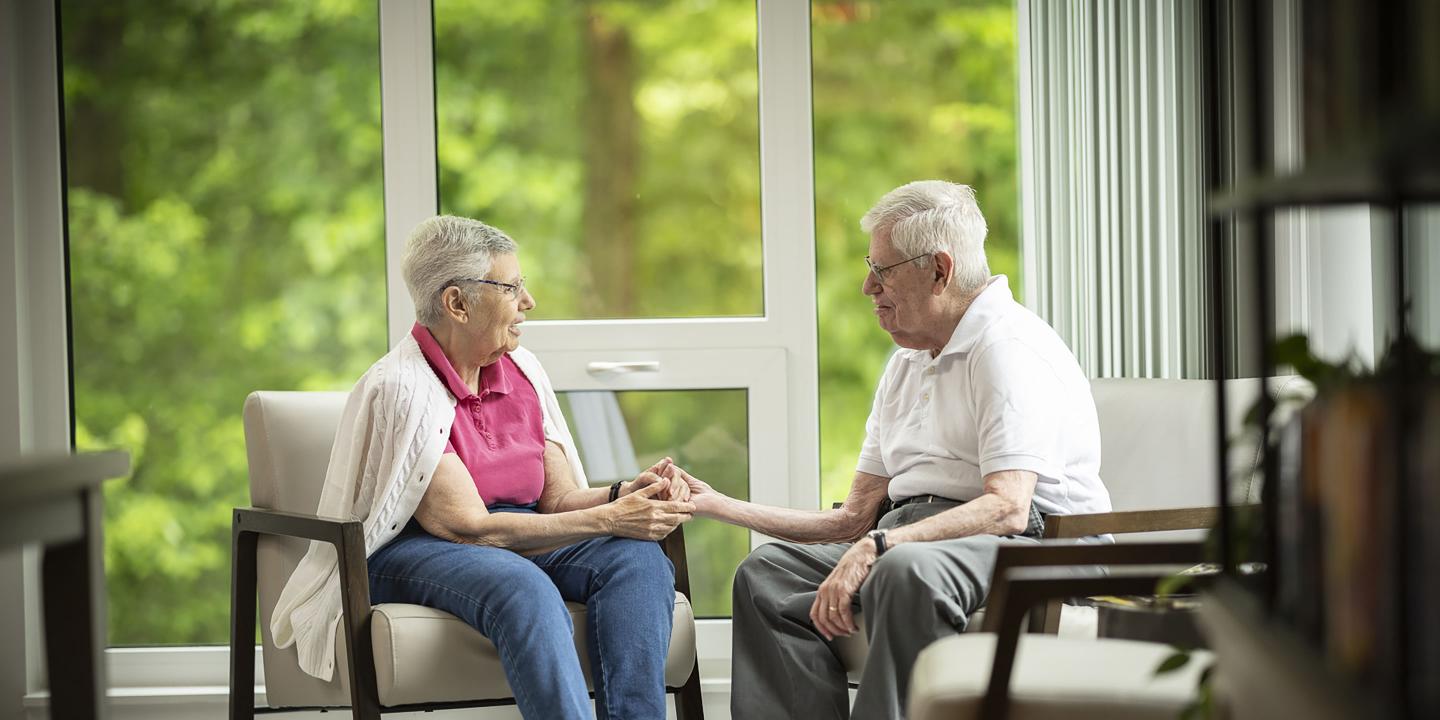 An older couple talk while sitting and holding hands.