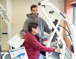 A CCB resident uses a piece of exercise equipment with the assistance of a trainer.