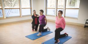 Two women residents do lunges on workout mats while one gets help from an instructor 