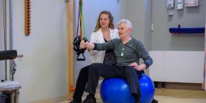 Patient sitting on a ball and doing an arm exercise under the guidance of a medical staff person.