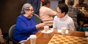 Two women sit at a table drinking coffee and talking at Simon C. Fireman Community in Randolph, MA