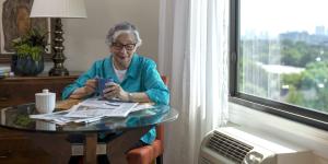 Older woman sitting at a table reading newspaper