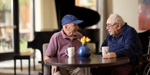 Two older men sitting together at a table in a lounge area.