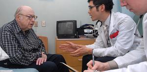 Older man sitting and talking with two doctors.