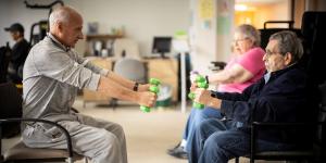 Physical therapist showing older adults exercises to do with dumbbells while sitting down