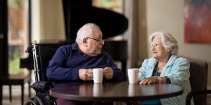 Older man sitting in a wheelchair at a table having coffee with an older woman