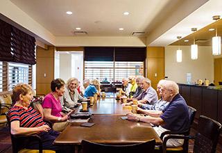 A group of NewBridge residents sit around a table talking and drinking coffee.