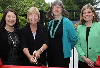 Four women stand in front of a red ribbon at a ribbon-cutting ceremony
