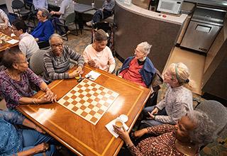 A diverse group of seniors sits at a table, laughing and chatting at Simon C. Fireman Community in Randolph, MA