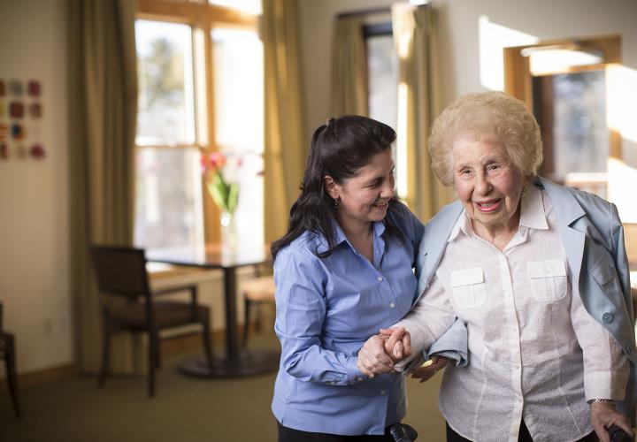 An assisted living resident at NewBridge on the Charles receives help with the tasks of daily living in her bright apartment.