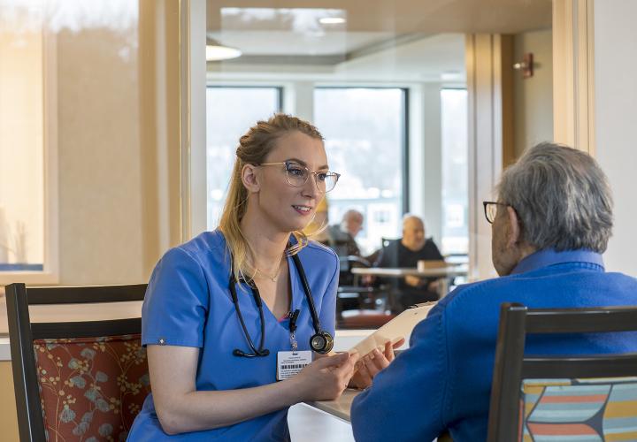 Caregiver wearing blue talking to patient in long-term chronic care sitting down at table