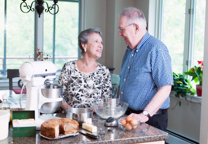 Man and woman stand together next to a counter with a mixer and baking ingredients in the kitchen of their independent living apartment.