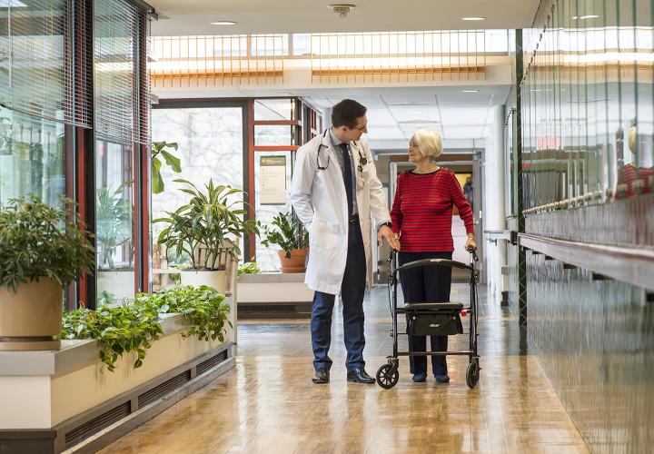 Compassionate doctor talking with older woman using walker in Hebrew Rehabilitation Center hallway