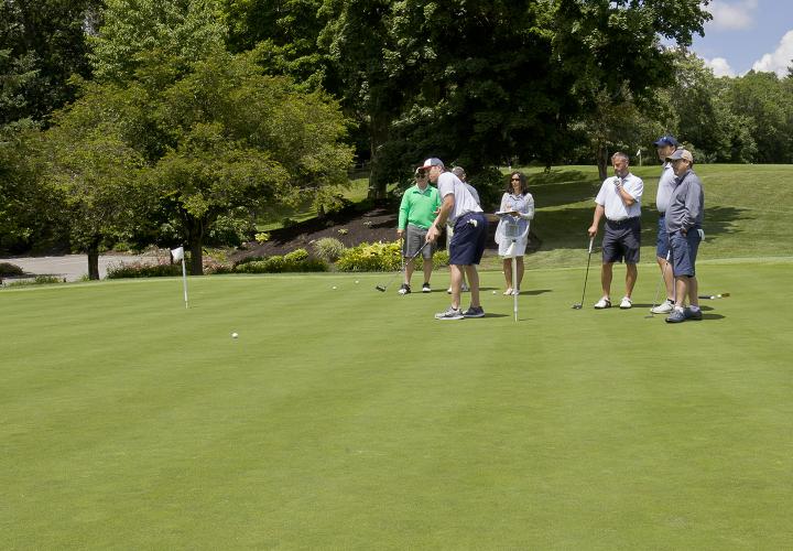 Beautiful day with a golfer on the green with several other golfers in background